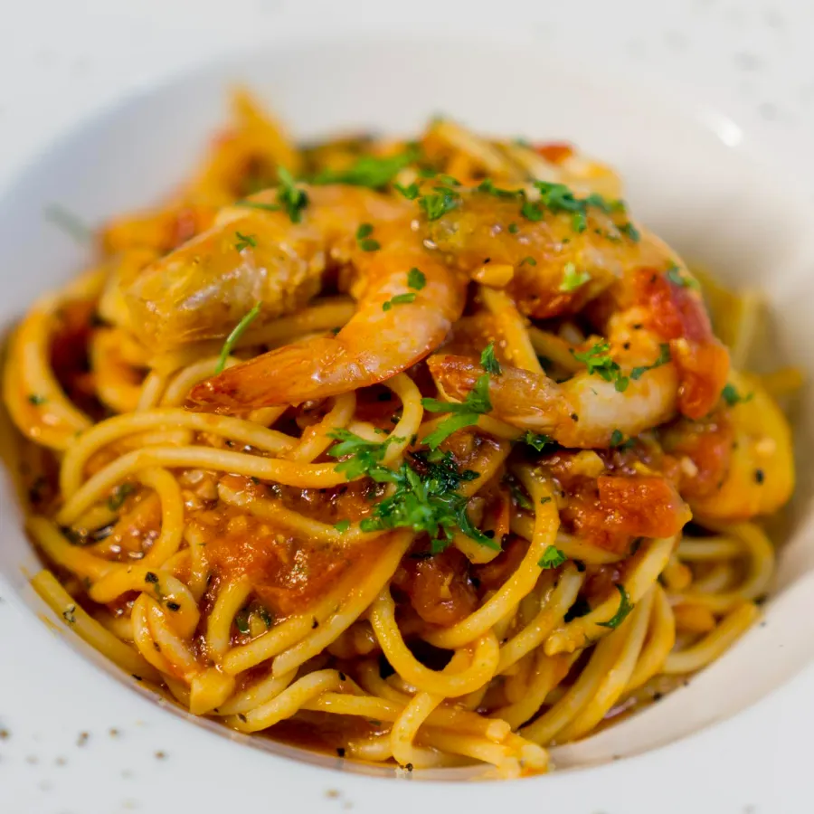 spaghetti served in a white plate with some red sauce and shrimps served on it