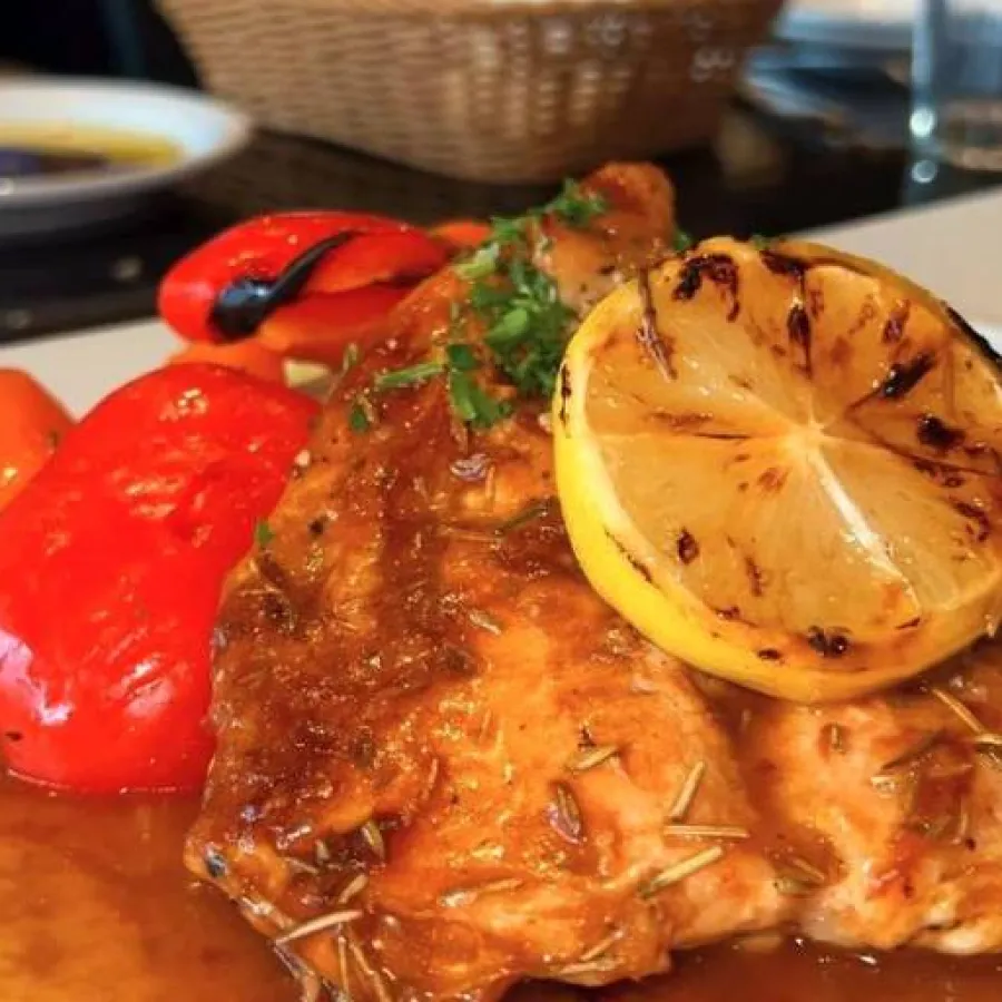 chicken made in sauce presented in a white plate with half lemon and some tomatoes in it