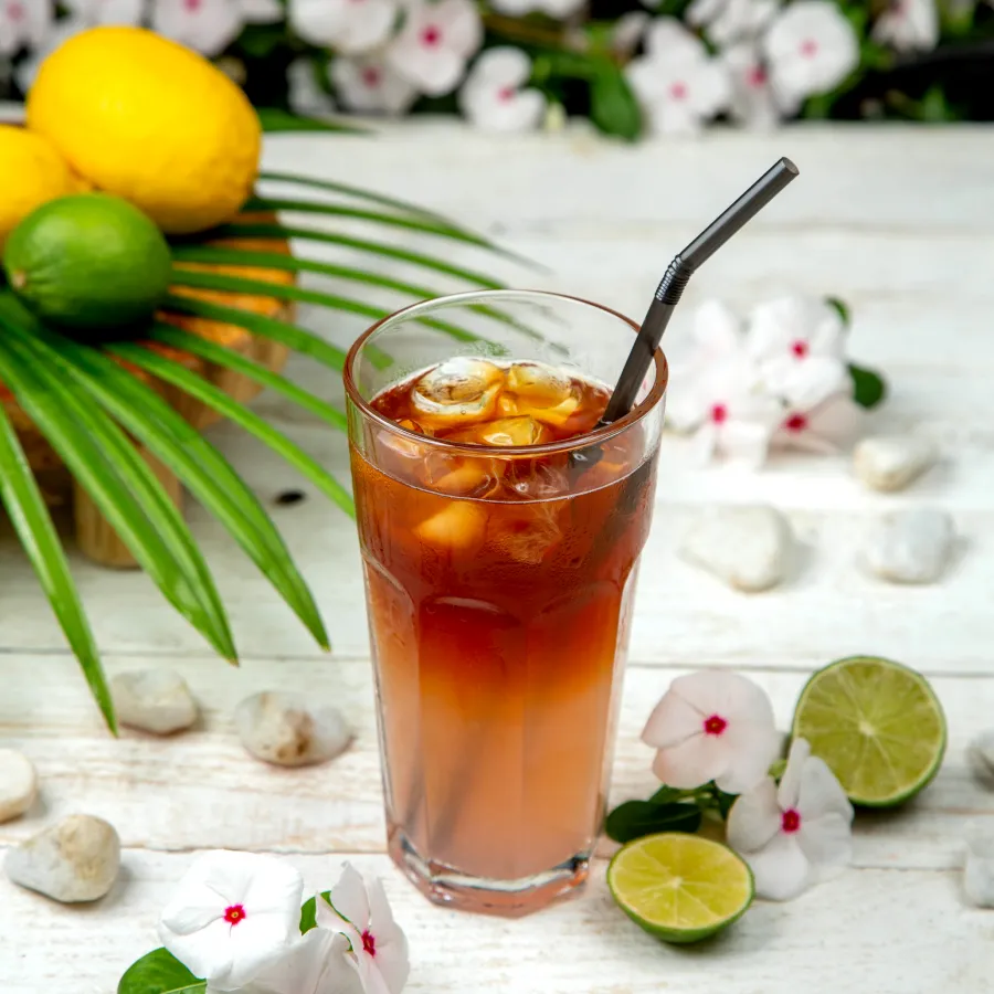 A glass with brown colour drink in it and some ice cubes and a straw