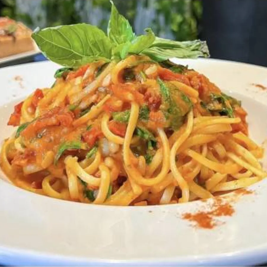 spaghetti made in red sauce with a basil leaf on the top and served in a white plate